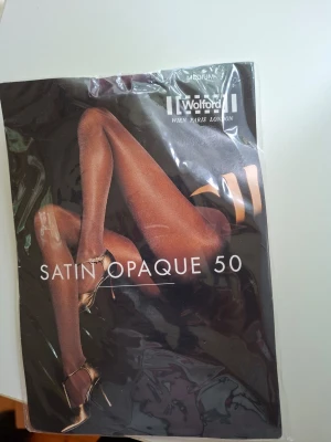 Wolford Satin Opaque 50 aubergine - Wolford Satin Opaque 50 strumpbyxor i färgen aubergine. Täckande och mjuka med satinfinish, perfekt för en snygg och stilren look. Strumpbyxorna är i storlek medium och har en elegant lyster.