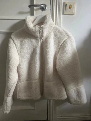 Vit teddyjacka från Gina Tricot - Supermjuk och fluffig vit teddyjacka från Gina Tricot med hög krage och dragkedja framtill. Jackan har lång ärm och är perfekt för att hålla värmen under kyliga dagar. Enkel och stilren design som passar till det mesta.