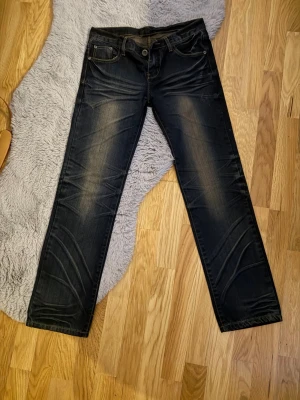 Mörkblå raka jeans med slitningar - Snygga mörkblå jeans med raka ben och diskreta slitningar framtill. Klassisk femficksmodell med kontrastsömmar och knappgylf. Jeansen har en tvättad look och är tillverkade i denim, perfekt för en avslappnad stil.