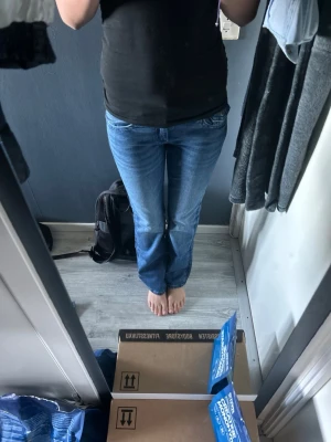 Blå bootcut jeans med broderade fickor - Säljer ett par blå bootcut jeans med snygg tvätt och broderade bakfickor med rosettdetaljer. Jeansen har klassisk femficksmodell, knappgylf och raka ben. Perfekta för dig som gillar en avslappnad men ändå trendig stil.