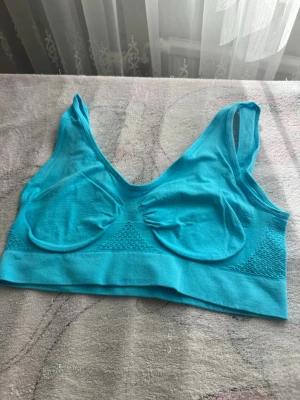 Turkos sömlös bh i stretchigt material - Säljer en turkos bh utan bygel med breda axelband och sömlös design. Bh:n har lätt formade kupor och är tillverkad i ett mjukt, stretchigt syntetmaterial som ger en bekväm passform. Perfekt för dig som vill ha en enkel och smidig bh.