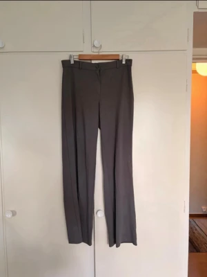Mörkgrå raka kostymbyxor - Snygga mörkgrå kostymbyxor med rak passform. Byxorna stängs med knapp och dragkedja. Materialet är polyester, elastan och viskos och är superskönt!! Känns nästan mer som mjukisbyxor.