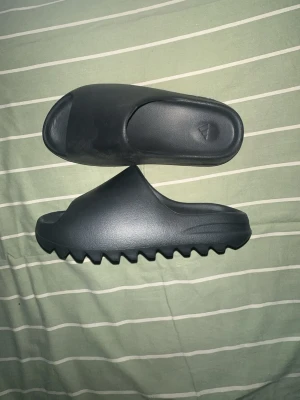 Svarta adidas slides - Säljer ett par svarta tofflor i slides-modell med bred rem över foten och kraftigt räfflad sula. Tillverkade i ett mjukt och flexibelt material som ger skön komfort. Perfekta för chill dagar hemma eller snabba ärenden.