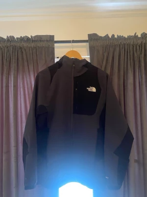 Svart vindjacka från The North Face - Snygg svart vindjacka från The North Face med dragkedja framtill och huva. Jackan har logga på bröstet och ryggen, samt paneler i mörkare nyanser för en sportig look. Perfekt för blåsiga dagar och outdoor-aktiviteter. Priset är förhandlingsbart!