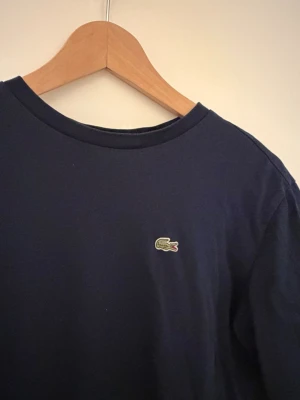 Mörkblå t-shirt från Lacoste - Klassisk mörkblå t-shirt från Lacoste med den ikoniska krokodilloggan broderad på bröstet. 