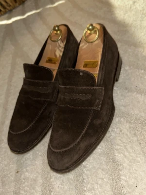 Mörkbruna mocka loafers - Säljer ett par stilrena mörkbruna loafers i mjuk mocka. Skorna har klassisk penny loafer-design med rundad tå och diskret söm längs ovandelen. Perfekta för dig som gillar tidlös och clean stil. Storlek 40 men är stor i storleken så passar någon som har runt 42🤎 Säljer då dom är för stora för sambon och därav ej kommer till användning tyvärr. Superfina till exempelvis födelsedagar, bröllop, dop eller vid finare/festligare tillställningar👞💼💖✨