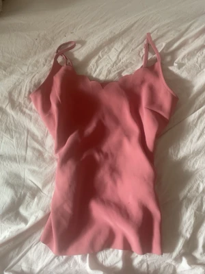 Rosa linnetopp från Ted Baker - Supersöt rosa linnetopp från Ted Baker med justerbara axelband och vågig kant upptill. Perfekt att styla med jeans eller kjol för en trendig look. Materialet känns mjukt och lätt mot huden.