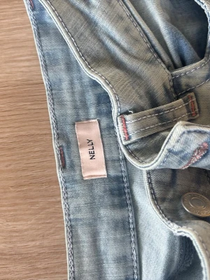Ljusblå raka jeans med slitningar - Säljer ett par ljusblå jeans med raka ben och slitna detaljer vid knäna. Jeansen har klassisk femficksmodell och hög midja. Tillverkade i denim för en avslappnad och trendig look.