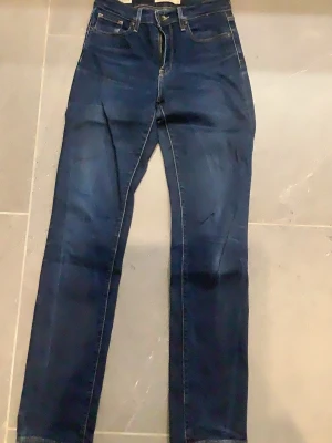 Mörkblå raka LEVI’S jeans med hög midja - Snygga mörkblå LEVI’S  jeans med raka ben och hög midja. Klassisk femficksmodell med kontrastsömmar och dragkedja fram. Jeansen har en tidlös look och passar perfekt till olika stilar. Materialet är denim i bomull.