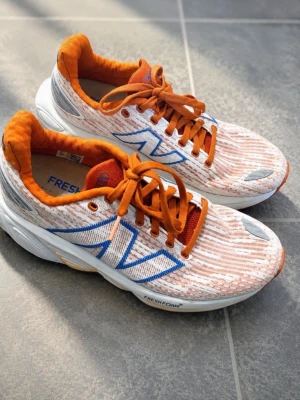 New Balance skor. Vita och orange sneakers med blå detaljer - New Balance skor. Stl 36.5. Säljer ett par sneakers i vitt och orange med blå detaljer och orange snörning. Skorna har en sportig design med vadderad insida och Fresh Foam-sula för extra komfort. Yttermaterialet är textil med mönstrad ovandel och reflexdetaljer baktill. Använda en gång så i nycskick! Jag betalade 1900kr säljes för 1000kr