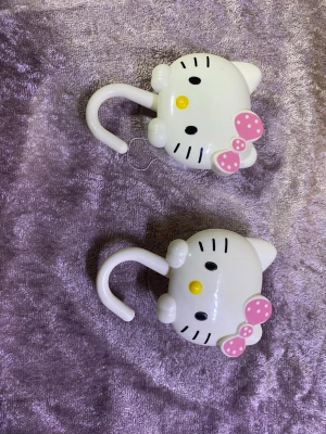 2 st Hello Kitty krokar med sugpropp - Två söta krokar i form av Hello Kitty-huvuden med rosa prickiga rosetter. Krokarna är vita och har sugpropp på baksidan för enkel upphängning på släta ytor. Perfekta för att hänga upp accessoarer eller småsaker i rummet. Helt ny 