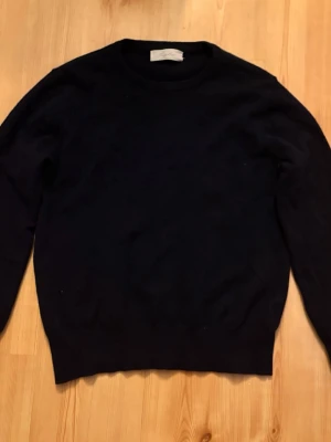 Svart stickad tröja från Sayless - En klassisk svart stickad tröja från Sayless med rund halsringning och långa ärmar. Perfekt för lager-på-lager och enkel att matcha med olika outfits. Tröjan har en stilren och tidlös design. Det är en tröja I cashmere. Stolen s passar dig som är ungefär 170/175 cm lång.