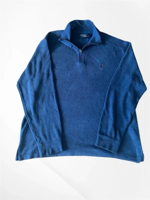 Polo Ralp Lauren Blå stickad tröja med halv dragkedja - Mysig blå stickad tröja från Polo Ralph Lauren med halv dragkedja och klassisk krage. Tröjan har lång ärm och den ikoniska broderade loggan på bröstet. Perfekt för lager på lager och en avslappnad men stilren look.