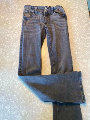 Blå bootcut jeans med dubbla knappar - Snygga blå bootcut jeans med dubbla knappar i midjan och klassiska fem fickor. Jeansen har en lätt tvättad look och breda hällor för bälte. Perfekta för dig som gillar en avslappnad men trendig stil.