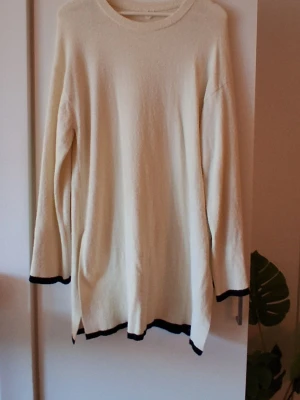 Vit stickad tröja med svarta kanter Arket Medium  - Långärmad vit stickad tröja med svarta detaljer vid ärmslut och nederkant. Tröjan har en avslappnad passform och rund halsringning. Perfekt för dig som gillar enkel och stilren design.