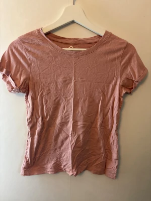 Ljusrosa basic t-shirt i bomull - En enkel ljusrosa t-shirt med rund hals och korta ärmar. Tillverkad i mjuk bomull som känns skön mot huden. Perfekt att matcha med jeans eller kjol för en avslappnad look.