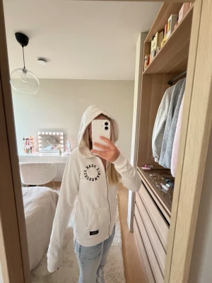 Vit hoodie från Peak Performance XS - Säljer en vit hoodie från Peak Performance i storlek XS. Hoodien har huva, ficka framtill och svart texttryck på bröstet. Tillverkad i mjukt och skönt material, perfekt för chill dagar eller när du vill ha en clean look.🩷