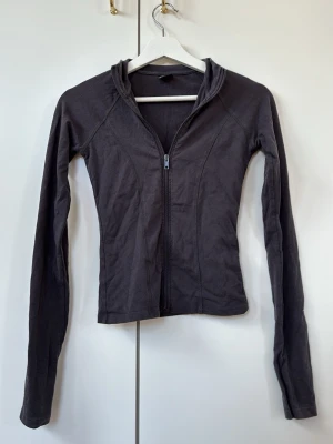 Mörkgrå ziptröja perfekt för träning  - Slimmad mörkgrå ziptröja med långa ärmar och tumhål. Tröjan har en figurnära passform och är tillverkad i ett mjukt, stretchigt material. Perfekt för träning, promenader eller bara som en kofta.