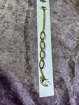 Guldigt armband med stora länkar - Snyggt armband i guldfärgad metall med tre stora ovala länkar, varav två är dekorerade med glittrande stenar. Kedjan har justerbar längd och ett klassiskt spänne. Perfekt för dig som gillar statement-smycken och vill sticka ut.