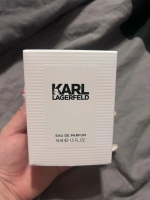 Karl Lagerfeld Eau de Parfum 45ml - Säljer en stilren parfym från Karl Lagerfeld i en vit, strukturerad kartong. Flaskan innehåller 45 ml Eau de Parfum. Förpackningen har en modern och minimalistisk design med svart logotyp på framsidan. Halva kvar.
