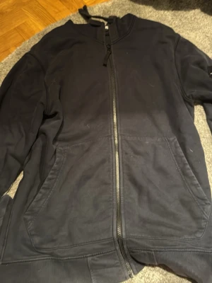 Blå zip hoodie från Stone Island - Snygg blå hoodie från Stone Island med dragkedja framtill och två stora fickor. Klassisk patch med logga på vänster ärm. Tillverkad i mjukt bomullsmaterial och har ribbade muddar vid ärmslut och nederkant. Perfekt för en avslappnad streetwear-look.