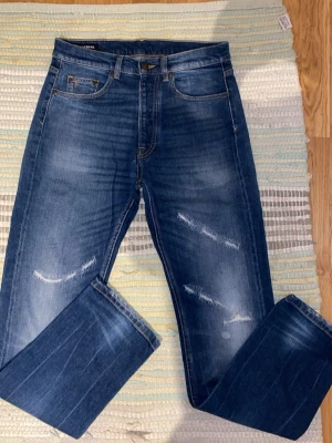 J.Lindeberg jeans straight - Säljer ett par blå jeans från J.Lindeberg med snygga slitningar. Jeansen har raka ben och är tillverkade i denim med en tvättad look. Perfekta för en avslappnad och trendig stil. Aldrig använda! Köpta i J.Lindebergs butik. Priset kan diskuteras!