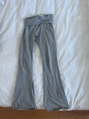 Grå bootcut leggings med låg midja - Säljer ett par grå leggings med bootcut och bred, vikbar midja. De är stretchiga och sitter skönt på kroppen, perfekta för en avslappnad och trendig look. Materialet känns mjukt och följsamt, och färgen är en klassisk ljusgrå.