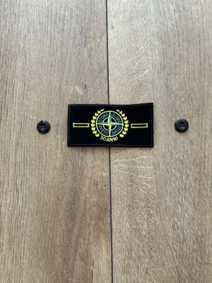 Stone Island Patch / Badge – Limited Edition 30 Anni & knappar - Säljer en limiterad Stone Island-badge med texten "30 Anni" och tillhörande originalknappar, precis som på bilderna. Patchen är helt ny, oanvänd och i perfekt skick. En unik jubileumsmodell som passar perfekt som samlarobjekt eller reservdel till din jacka/tröja. 
