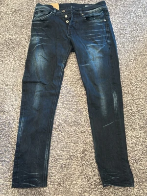 Mörkblå dondup George  - Säljer ett par mörkblå dondup i modellen George med snygga tvättade detaljer. Jeansen har smal passform. Perfekta för dig som gillar en trendig och avslappnad stil.