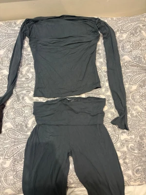 Mörkgrått set med långärmad topp - Säljer ett mörkgrön tvådelat set med långärmad, axelbandslös topp och matchande höga byxor. Materialet är mjukt och stretchigt, perfekt för en bekväm och stilren look. Passar dig som gillar minimalistisk stil. ( färgen ser grå ut men den e mörk coral grön) tröjan är M och byxorna S 