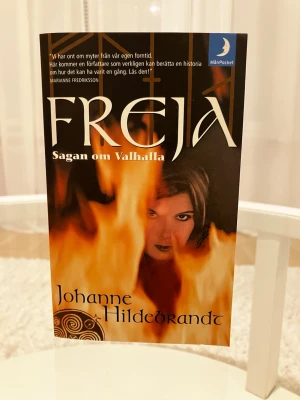 Freja - Sagan om Valhalla pocketbok - En spännande pocketbok av Johanne Hildebrandt, 'Freja - Sagan om Valhalla', med ett omslag i svart, orange och vitt. Boken handlar om fornnordiska myter, gudar och hjältinnor och utspelar sig i ett mytiskt Norden. Perfekt för dig som gillar äventyr och historia.