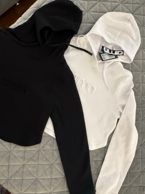 Cropade hoodies i vitt och svart - Två snygga cropade hoodies i vitt och svart med broderad text framtill. Båda har huva med dragsko och långa ärmar. Perfekta till ett par höga tights eller jeans för en chill och sportig look.