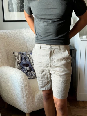Beiga linneshorts från Zara - Snygga beiga shorts från Zara i 100% linne. De har en klassisk passform med normal midja, knapp och dragkedja framtill samt fickor på sidorna. Perfekta för varma dagar och ger en clean och stilren look.
