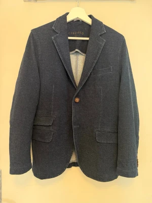 Mörkblå kavaj från Circolo - Tjena! Säljer denna unika kavaj från Circolo i ett denimliknande material. Kavajen har tre framfickor med lock och en bröstficka. Tillverkad i mjukt, stretchigt material som ger en avslappnad men ändå dressad look. | Storlek: 48 (S/M) | Skick: 9/10 | Nypris: 5999kr | Meddela gärna vid eventuella frågor! Mvh ResellGarms 