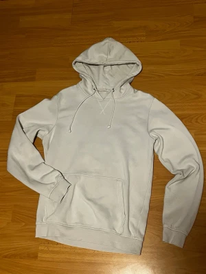 Vit hoodie från Pier One - Säljer en stilren vit hoodie från Pier One med klassisk huva och dragsnören. Hoodien har en stor magficka och ribbade muddar vid ärmar och nederkant. Perfekt för en avslappnad och enkel look.