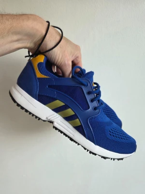 Adidas women running  - Snygga blå sneakers från Adidas med gula detaljer och klassiska ränder på sidan. Ovandelen är i mesh och syntetmaterial för bra andningsförmåga. Skorna har vita sulor och svarta yttersulor med bra grepp. Perfekta för dig som gillar sportig stil.