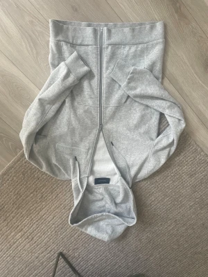 Ljusgrå hoodie från Peak Performance - Snygg ljusgrå hoodie från Peak Performance med dragkedja framtill och broderad logga på bröstet . Säljes då den har blivit för liten för mig , skick är som nytt 