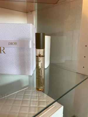 Rituals velvet Aura parfymolja - Säljer en stilren parfym i en smal, transparent glasflaska med brun kork. Flaskan har guldiga detaljer och text på sidan. Perfekt att ha med i väskan för en fräsch doft när som helst.