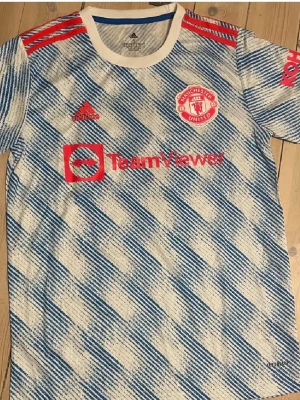 Manchester United  - Snygg Manchester United bortatröja från Adidas med Ronaldo 7 på ryggen. Tröjan har blåvitt mönster, röda detaljer och klubbmärke samt sponsortryck på bröstet.