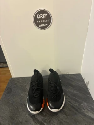 Hermees sneakers svarta - Snygga svarta sneakers med stickad ovandel, vita sulor och en cool orange detalj på sidan. Skorna har rund tå, svarta skosnören och dragflikar både fram och bak för enkel påtagning. Perfekta för dig som vill ha en modern och sportig look.