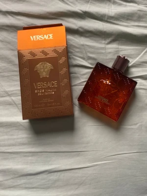 Versace Eros Najim Parfum 100ml - Versace Eros Naim Parfum i en snygg, fyrkantig glasflaska med bronsfärgad finish och elegant mönster. Flaskan har Versaces ikoniska Medusa-huvud på framsidan och kommer med matchande lyxig förpackning. Innehåller 100 ml parfym.