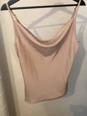 Beige linnetopp med tunna band - Säljer en stilren beige linnetopp med tunna justerbara axelband och snygg draperad urringning. Toppen har en mjuk, slät yta och är perfekt för varma dagar eller lager på lager. Enkel att matcha med olika stilar.