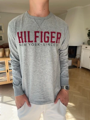 Tommy Hilfiger långärmad T-shirt broderat tryck herr - Klassisk Tommy Hilfiger sweatshirt i grått med stort broderat HILFIGER-tryck över bröstet. Stilren vintage/preppy känsla med fina detaljer och ribbade muddar. Ett riktigt lättmatchat plagg som lyfter outfiten. 🔥  #TommyHilfiger #Hilfiger #Sweatshirt #Preppy #Vintage #90s #Y2K #Herrmode #Classic #Streetwear