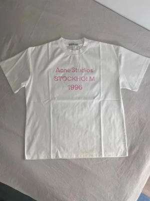 Acne Studios Stockholm T-shirt  - Vit Acne Studios T-shirt med rosa text. Helt ny, endast testad. Orginalpåse och tagg fås med. 