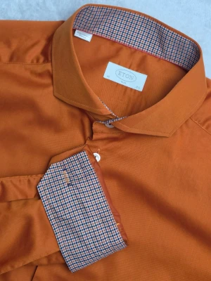 Eton Slim skjorta orange/bränd storlek 44 / 17½ Oanvänd - Stilren enfärgad skjorta från Eton i Slim-passform. Elegant bränd orange nyans med kontrasttyg i krage och manschetter. Tillverkad i 100% bomull och producerad i Europa. Passar lika bra till kostym som till chinos eller jeans.  Storlek 44 / 17½ Slim Fit  Oanvänd.  Mått Bröstbredd: ca 57 cm Plagglängd: ca 77 cm Axelbredd: ca 49 cm Ärmlängd: ca 70 cm  Material 100% bomull  Cut away-krage med kontrasttyg i krage och manschetter.