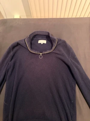 Mörkblå ziptröja från Friday Casual - Mörkblå ziptröja från Friday Casual med hög krage och grovstickad struktur. Tröjan har dragkedja framtill och ribbade muddar vid hals och ärmslut. Perfekt för en avslappnad och stilren look.