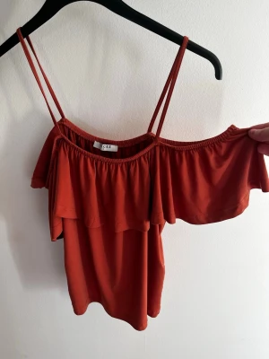 Rostfärgad volangtop från Pieces - Säljer en snygg rostfärgad topp från Pieces med tunna dubbla axelband och volangdetalj över bysten. Toppen har en luftig passform och är tillverkad i ett mjukt, stretchigt material som känns skönt mot huden. Perfekt för varma dagar eller lager på lager.