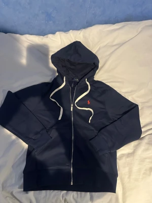 Mörkblå hoodie från Polo Ralph Lauren - Snygg mörkblå hoodie med dragkedja från Polo Ralph Lauren.  Fick den som present men har large i storlek och den passar inte. Storlek M. Sprillans ny, lappen är kvar men avklippt.