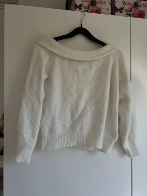 Vit off shoulder stickad tröja - Mysig vit stickad tröja med bred off shoulder-krage och långa ärmar. Tröjan har ribbstickade muddar vid ärmslut och nederkant, vilket ger en snygg och avslappnad look. Perfekt för dig som gillar en enkel men trendig stil.