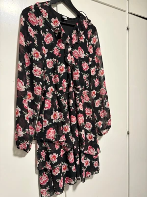 Svart blommig klänning och en koral rosa skjorta  - Dessa 2 för 300kr och en för 150kr. Supersöt svart kortklänning med rosa och vita blommor. Klänningen har långa ärmar, volangdetaljer och en avslappnad passform. Perfekt för vår och sommar när du vill känna dig extra fin. Och en trendig korallrosa kavaj med öppen front och raka ärmar. Kavajen har två fickor framtill och en avslappnad passform. Perfekt för att addera färg till din outfit. Tillverkad i ett lätt tyg som ger en snygg siluett.
